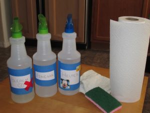 3 spray bottles, one with green top and red x, one with green top, and one with blue top and mickey mouse sticker, sponge, and roll of paper towels