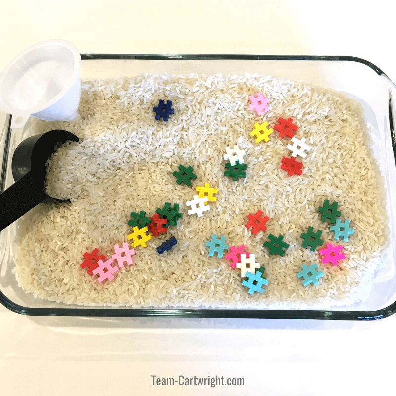 Rice sensory bin with funnel, measuring cup, and colorful waffle blocks